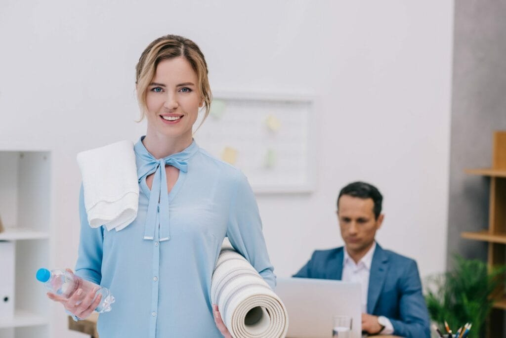 businesswoman with fitness equipment standing at modern office while her colleague working with