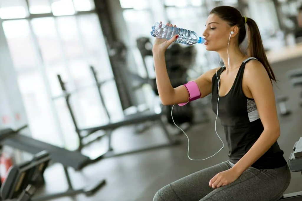 Attractive sport young woman drinking water while sitting and resting after workout
